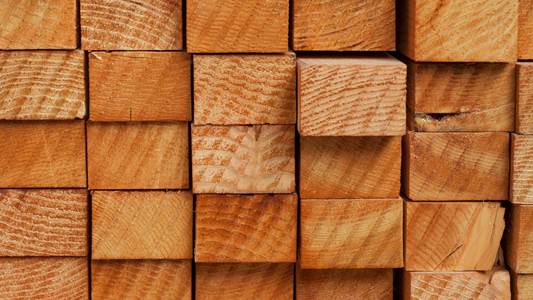 Stack of various outdoor wood types including cedar, redwood, and teak arranged in a rustic garden workspace